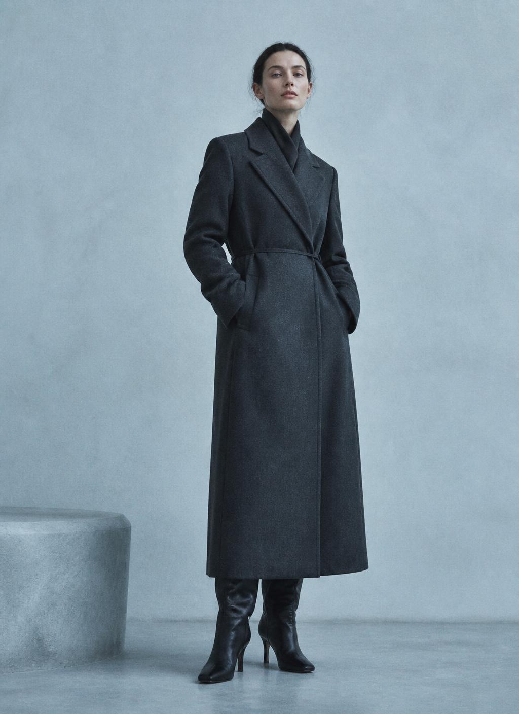 Tall woman in a long structured charcoal winter coat, frost-tinted studio